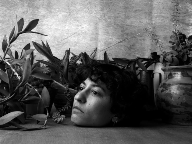 monochrome photograph with a disembodied head, some foliage, and a jar
